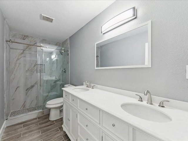 bathroom featuring toilet, a marble finish shower, wood finished floors, and a sink