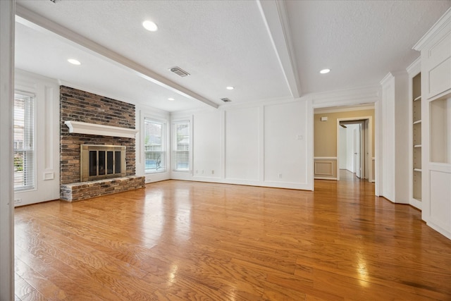 1415 Stependale Dr, Katy, TX 77450 - unfurnished living room featuring beam ceiling, a textured ceiling, a decorative wall, light wood-style floors, and built in shelves