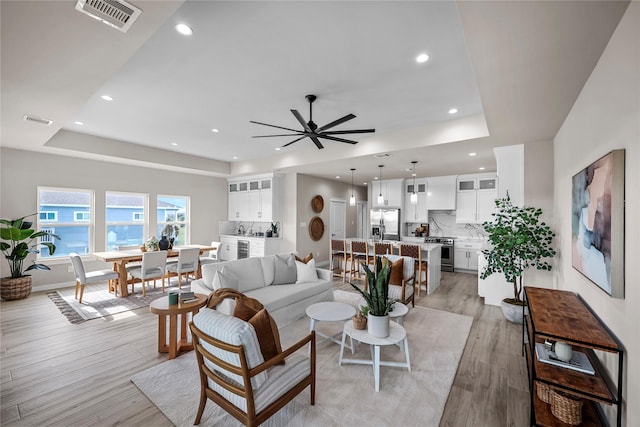 living room featuring a tray ceiling, a ceiling fan, light wood finished floors, recessed lighting, and baseboards