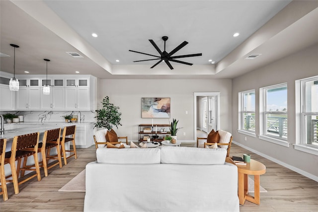 living room featuring a tray ceiling, recessed lighting, light wood-type flooring, ceiling fan, and baseboards