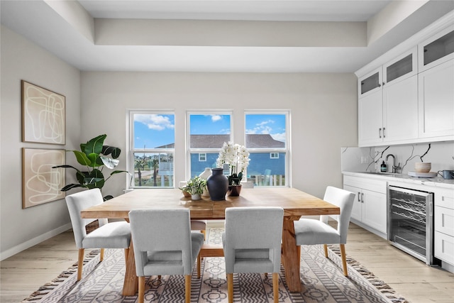 dining room featuring beverage cooler, light wood-style floors, bar with sink, and baseboards