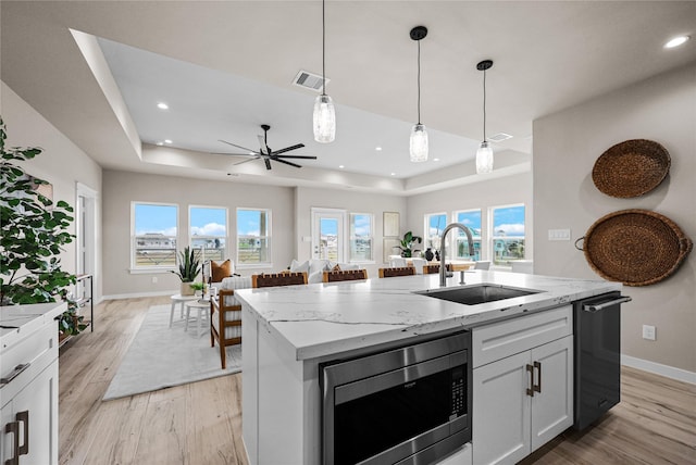 kitchen with stainless steel microwave, a sink, a raised ceiling, dishwashing machine, and light wood-style floors