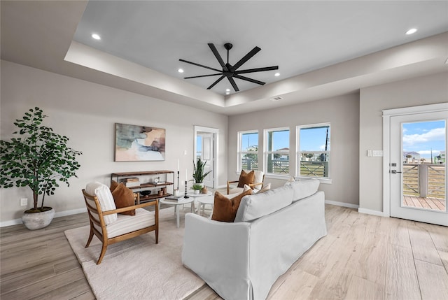 living room featuring a raised ceiling, light wood-style flooring, baseboards, recessed lighting, and a ceiling fan