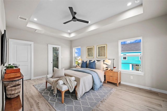 bedroom featuring a raised ceiling, light wood-style flooring, baseboards, recessed lighting, and a ceiling fan