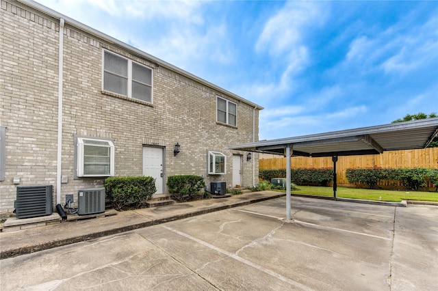 exterior space with central AC unit, brick siding, fence, and uncovered parking