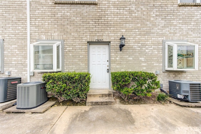view of exterior entry featuring central AC unit and brick siding