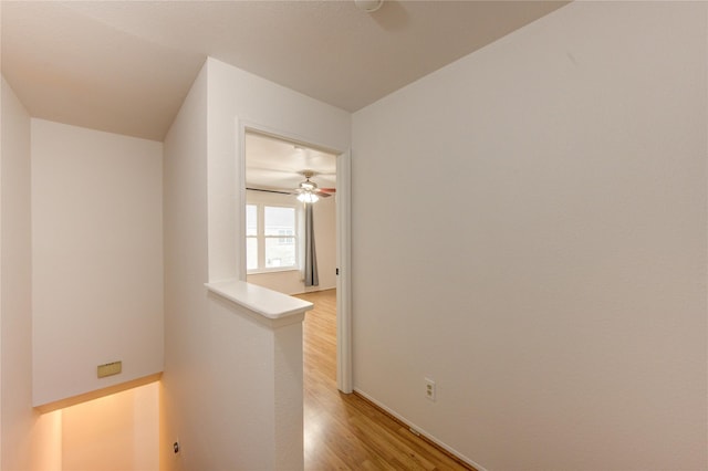 corridor with light wood finished floors, an upstairs landing, and baseboards