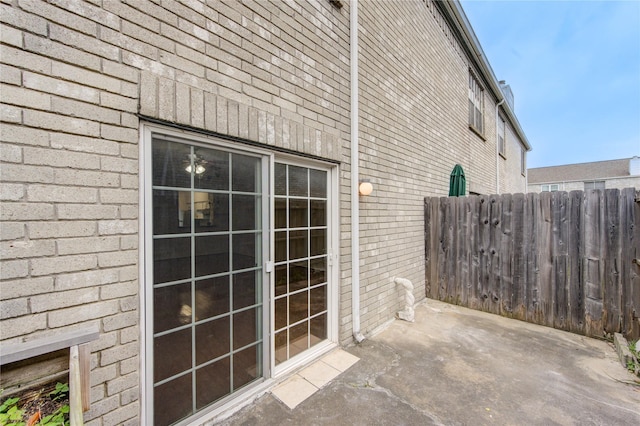 view of side of property featuring a patio, brick siding, and fence