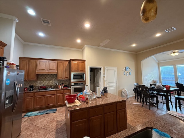 kitchen with backsplash, stainless steel appliances, brown cabinetry, and visible vents