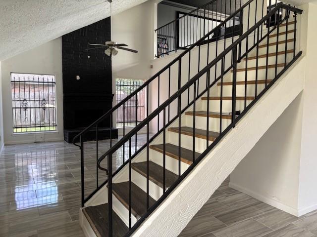 stairway with a ceiling fan, a textured ceiling, baseboards, a wealth of natural light, and vaulted ceiling