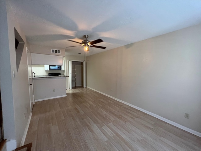 unfurnished living room with baseboards, visible vents, wood finished floors, and a ceiling fan