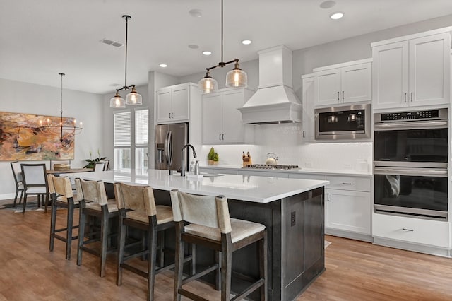 kitchen with visible vents, a sink, custom range hood, stainless steel appliances, and an island with sink