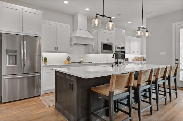 kitchen featuring a sink, stainless steel appliances, a center island with sink, custom exhaust hood, and light countertops