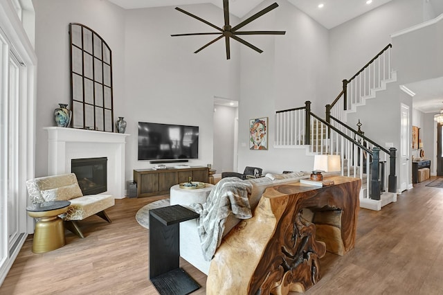 living room featuring ceiling fan, a towering ceiling, stairs, and wood finished floors