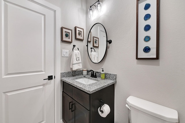 bathroom featuring toilet, vanity, and a textured wall