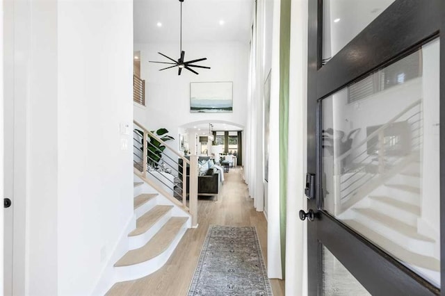 foyer entrance featuring ceiling fan, wood finished floors, arched walkways, stairway, and a high ceiling