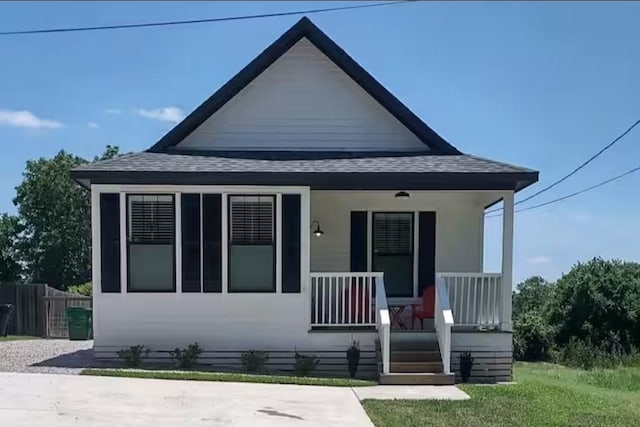 bungalow with a porch, roof with shingles, and fence