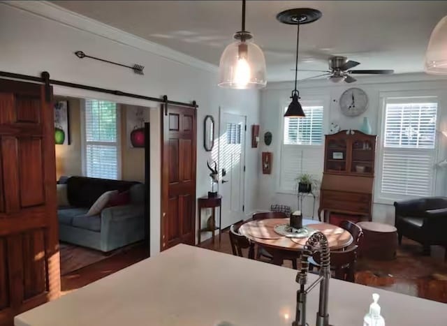 dining space with ornamental molding, a barn door, a ceiling fan, and wood finished floors