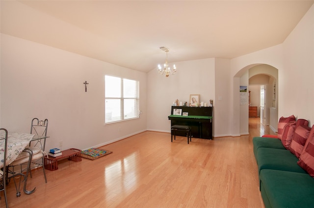 interior space with a chandelier, light wood-style flooring, arched walkways, and baseboards