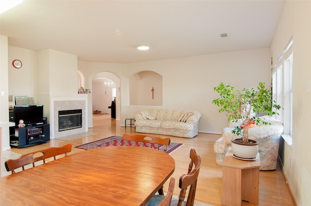 living area with light wood-type flooring, visible vents, arched walkways, baseboards, and a tiled fireplace