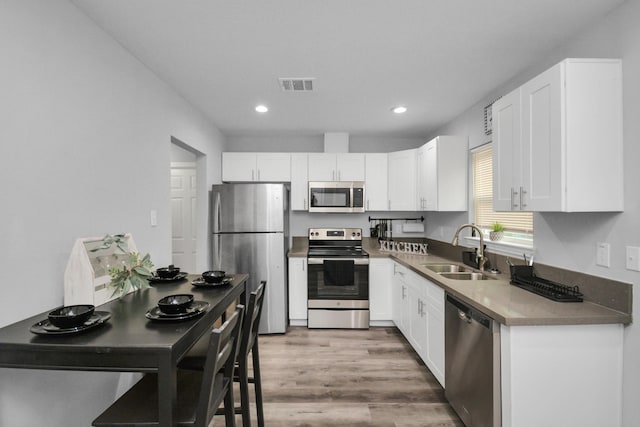 5410 Bataan Rd, Houston, TX 77033 - kitchen with appliances with stainless steel finishes, a sink, white cabinets, recessed lighting, and wood finished floors