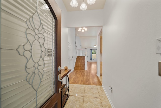 hallway with light tile patterned floors, stairway, a chandelier, and baseboards
