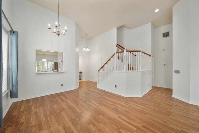 unfurnished room with an inviting chandelier, visible vents, high vaulted ceiling, wood finished floors, and stairway