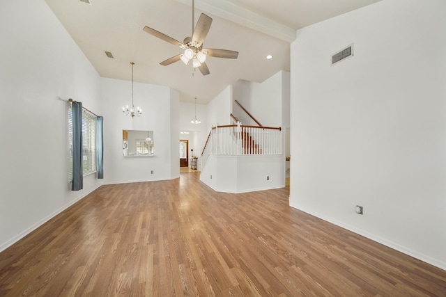 unfurnished living room with stairs, ceiling fan with notable chandelier, high vaulted ceiling, visible vents, and light wood-style floors