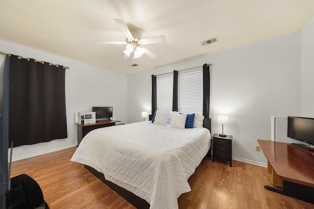 bedroom with a ceiling fan, visible vents, wood finished floors, and baseboards