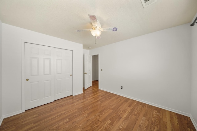 unfurnished bedroom with a closet, visible vents, wood finished floors, and baseboards