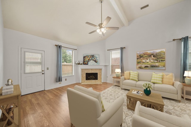living room with light wood finished floors, a tile fireplace, vaulted ceiling with beams, visible vents, and ceiling fan