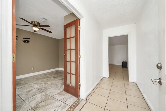 hallway with baseboards, light tile patterned flooring, and a textured ceiling