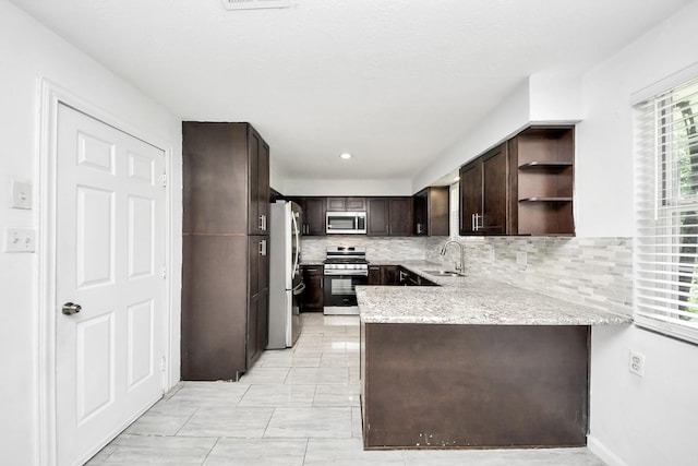 kitchen featuring stainless steel appliances, open shelves, dark brown cabinets, tasteful backsplash, and a sink
