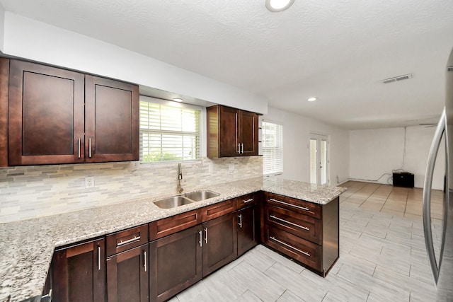kitchen with a sink, backsplash, a peninsula, light stone counters, and recessed lighting
