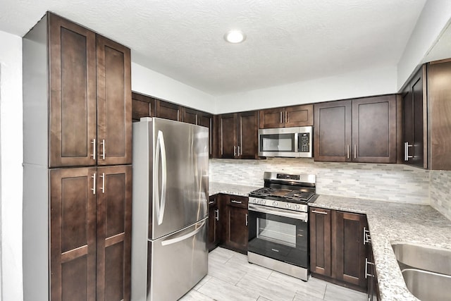 kitchen with stainless steel appliances, tasteful backsplash, dark brown cabinetry, and light stone countertops