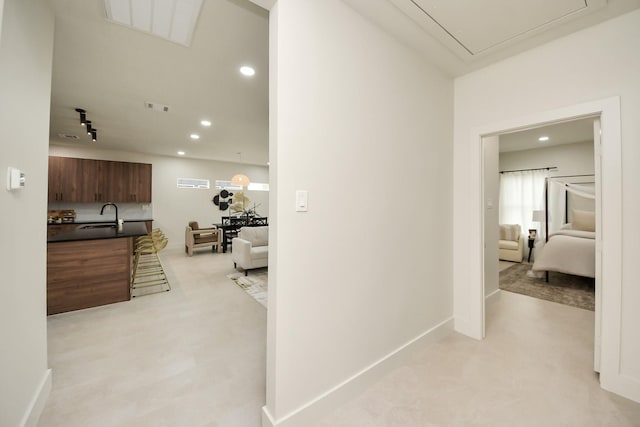 hall featuring attic access, recessed lighting, baseboards, and a sink