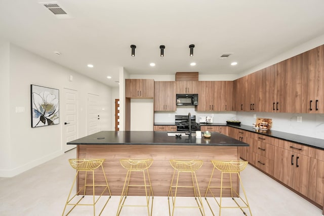 kitchen featuring black microwave, dark countertops, recessed lighting, range with gas cooktop, and a center island with sink
