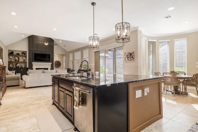kitchen with a sink, ceiling fan with notable chandelier, dark stone countertops, an island with sink, and stainless steel dishwasher