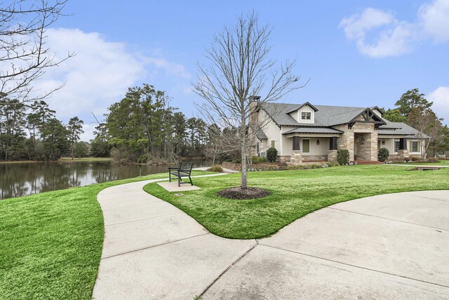view of front of house featuring stone siding, a water view, a chimney, and a front yard