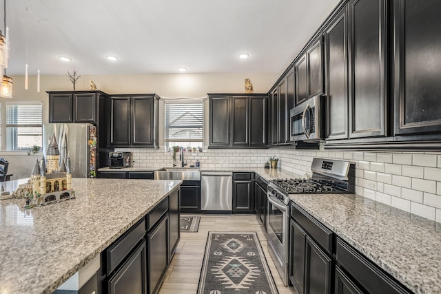 kitchen with light stone countertops, recessed lighting, a sink, tasteful backsplash, and appliances with stainless steel finishes