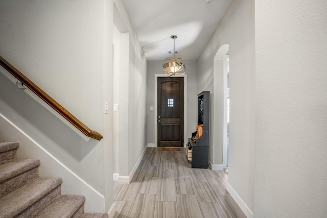 foyer entrance with arched walkways, stairway, light wood-style floors, and baseboards