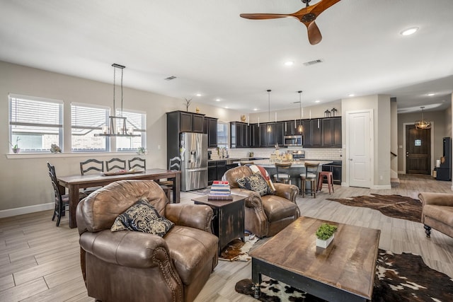 living room featuring light wood finished floors, ceiling fan with notable chandelier, visible vents, baseboards, and recessed lighting