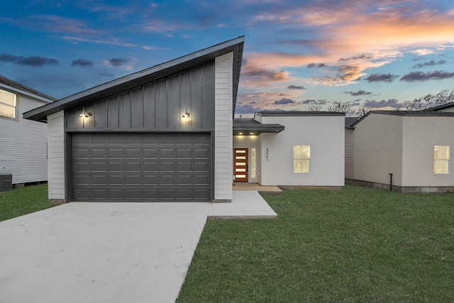 view of front of property with board and batten siding, concrete driveway, an attached garage, central AC unit, and a lawn