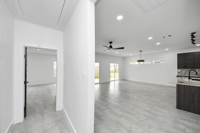 unfurnished living room with attic access, a sink, recessed lighting, a ceiling fan, and baseboards