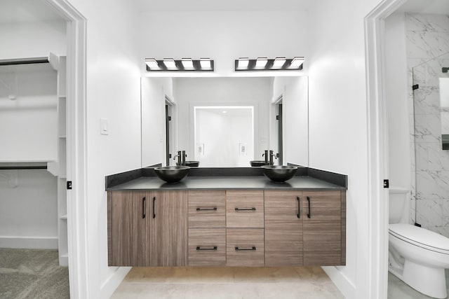 full bathroom featuring toilet, a marble finish shower, double vanity, a walk in closet, and baseboards