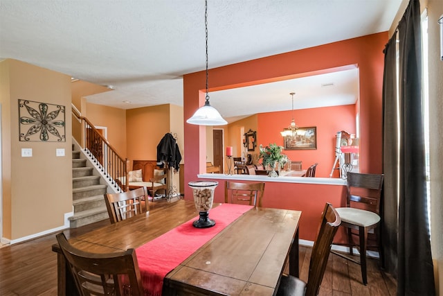 dining space with a textured ceiling, wood finished floors, baseboards, and stairs