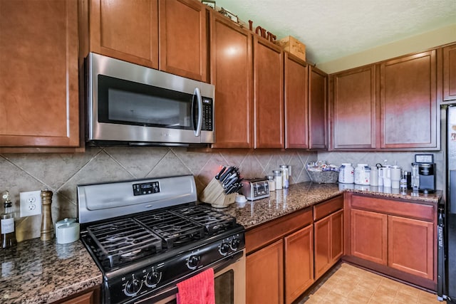 kitchen with stainless steel appliances, backsplash, dark stone countertops, and brown cabinets