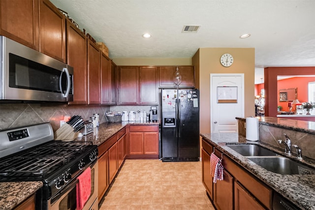 kitchen featuring dark stone countertops, a sink, stainless steel appliances, visible vents, and tasteful backsplash