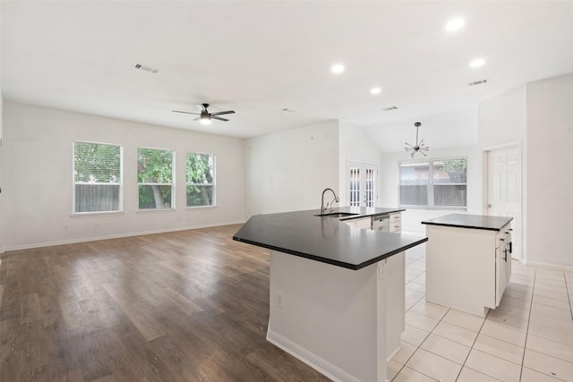 kitchen with visible vents, a sink, ceiling fan with notable chandelier, dark countertops, and an island with sink