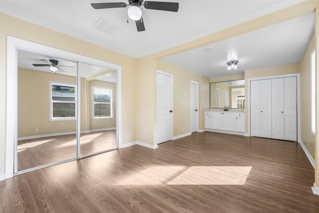 unfurnished bedroom with a ceiling fan, two closets, visible vents, baseboards, and dark wood-style floors